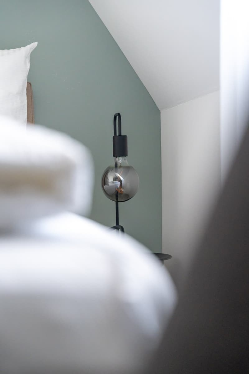 bed with white sheets, lamp, green wall