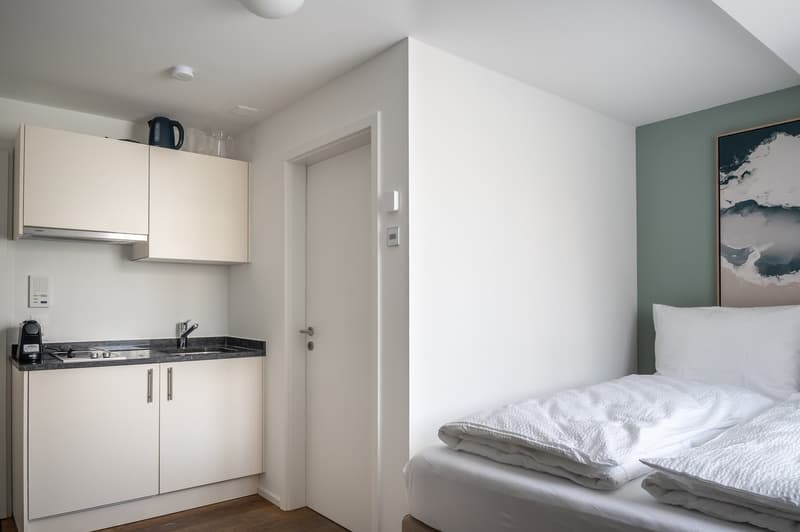 small room with a bed, a sink, a small stove, and a refrigerator