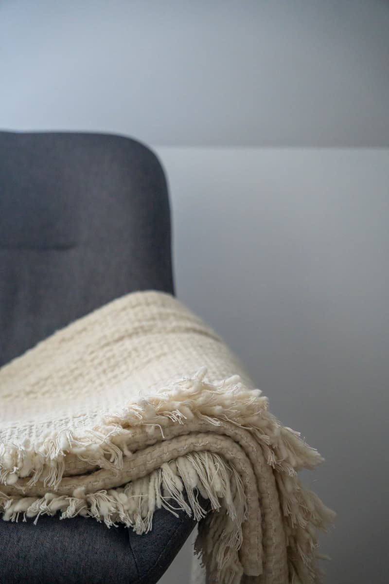 A beige blanket with fringes on a gray chair
