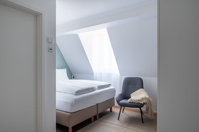 bedroom with bed, chair, rug, window, lamp, thermostat