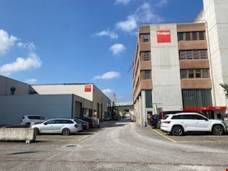 Multi-story commercial building with parking spaces in the front. The building has a modern, industrial design with a mix of brick and concrete materials. There are several vehicles parked in the lot in front of the building.