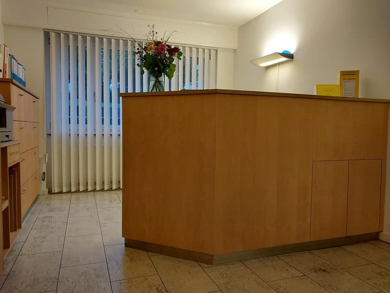 wooden desk with a lamp, white walls, white blinds, flower vase, cabinets, tiled floor