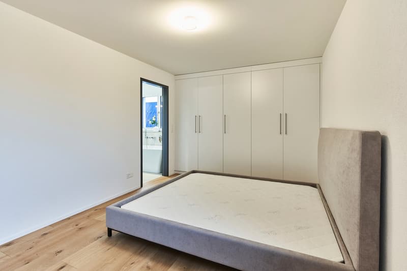 Spacious bedroom with white walls, hardwood floors, large built-in wardrobes, and a sliding glass door leading to a balcony or terrace.