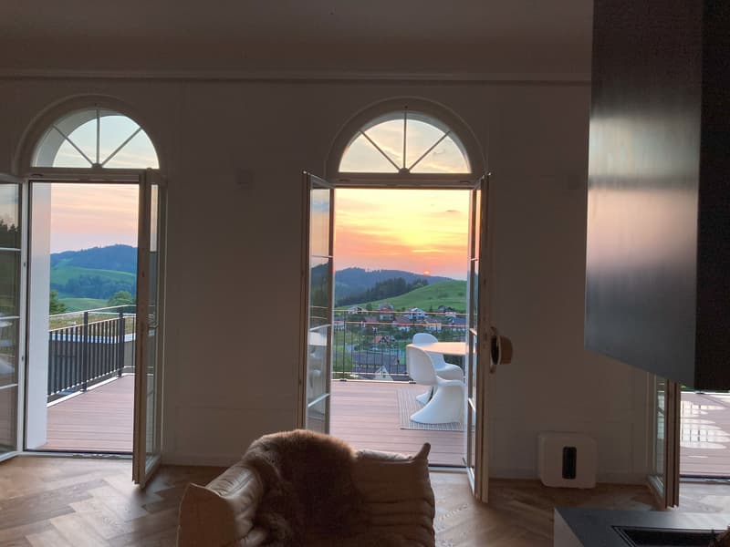 Double door entrance, balcony with round windows, large view to the sunset, white table and chairs on the balcony, fireplace, couch