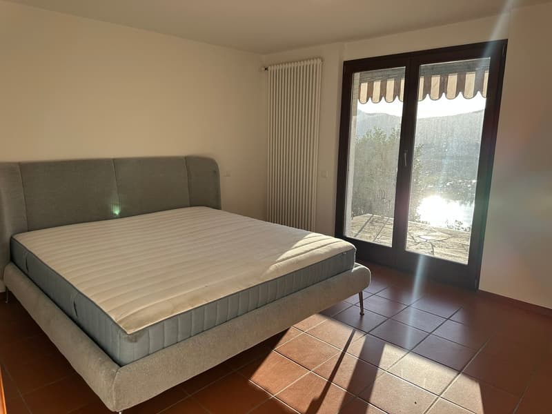 Spacious bedroom with a large bed, sliding glass door leading to a balcony or terrace, and tile flooring.