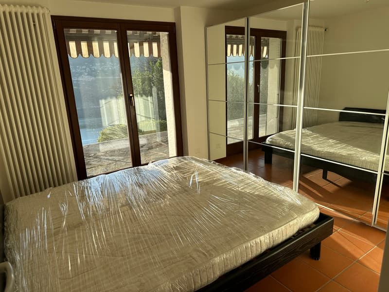 Spacious bedroom with large windows, sliding glass doors leading to a balcony or terrace, wooden bed frame, and mirrored closet doors.