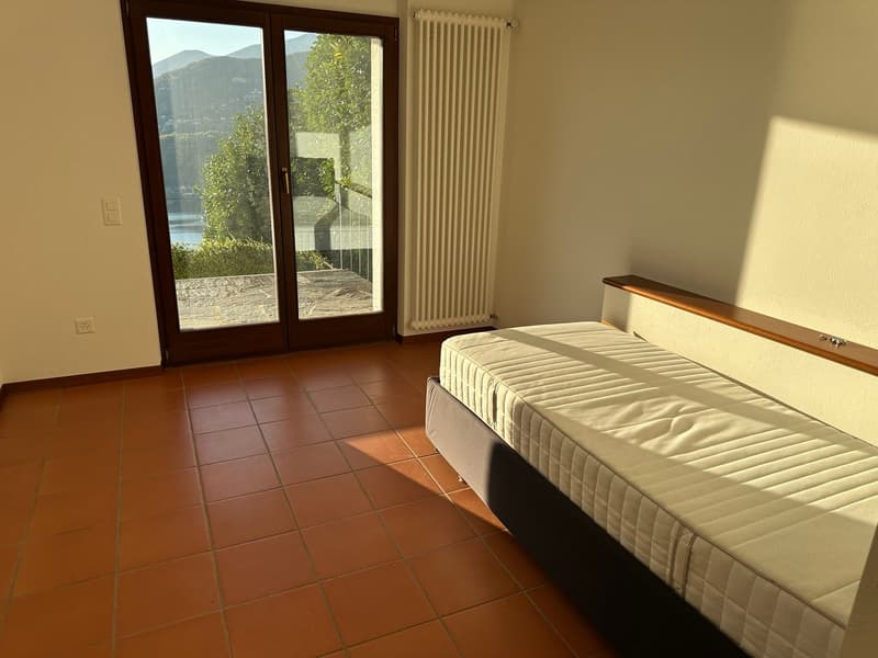 Spacious bedroom with large windows overlooking a balcony and scenic mountain view, hardwood floors, white walls, and a comfortable bed