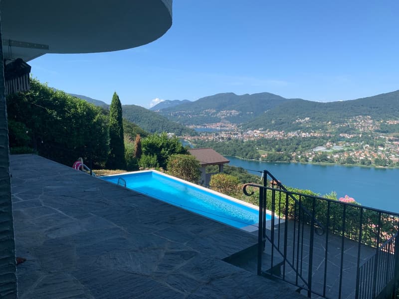 Luxury villa with an infinity pool overlooking a scenic lake surrounded by mountains and lush greenery