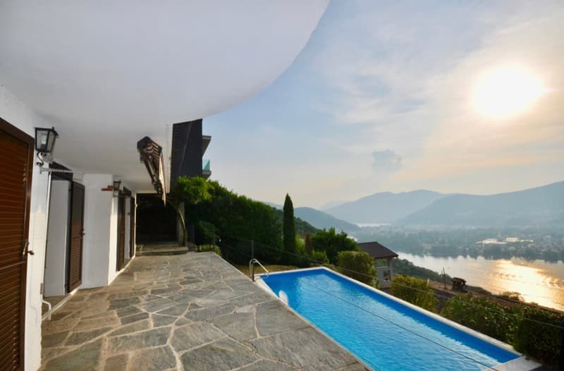 Luxury villa with a private swimming pool, surrounded by lush greenery and offering a stunning view of the mountains and lake in the background.