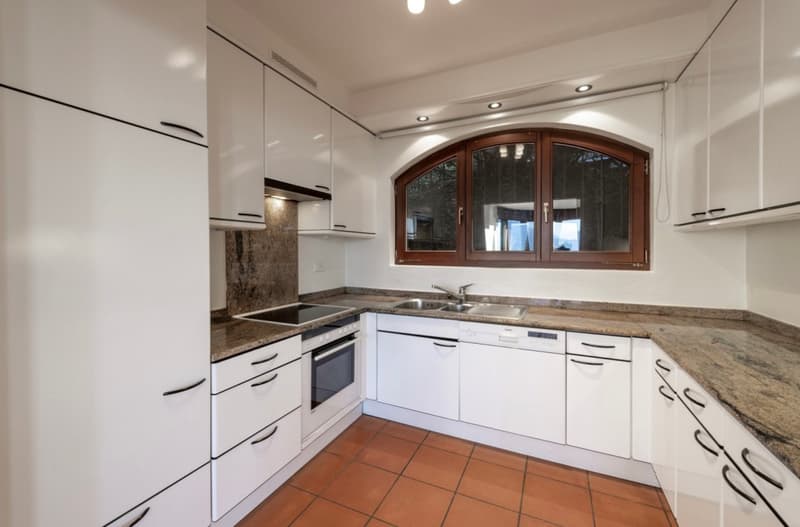Spacious kitchen with white cabinets, granite countertops, stainless steel appliances including a dishwasher, and a large arched window providing natural light.