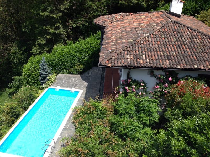 Two-story house with a red tile roof, surrounded by lush greenery and a swimming pool in the backyard.