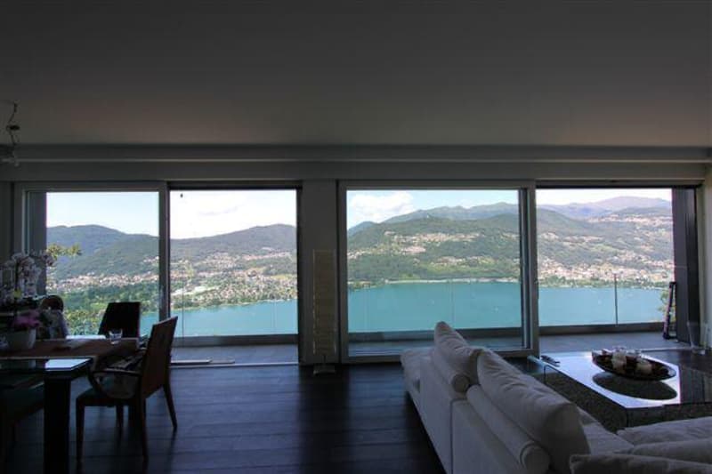 Large windows with a panoramic view of a lake and mountains in the distance, a couch facing the view, and a table with decor in the foreground.