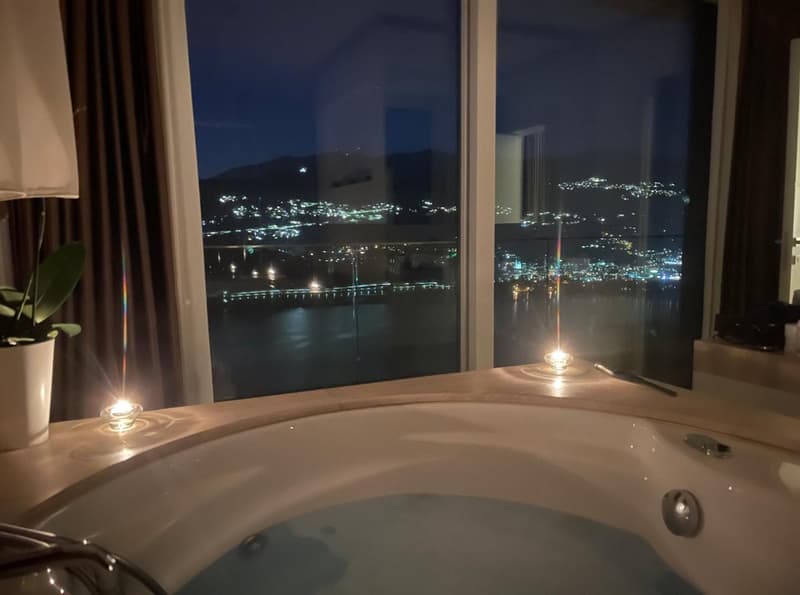 Bathtub with a view of a city skyline at night, with candles providing ambient lighting
