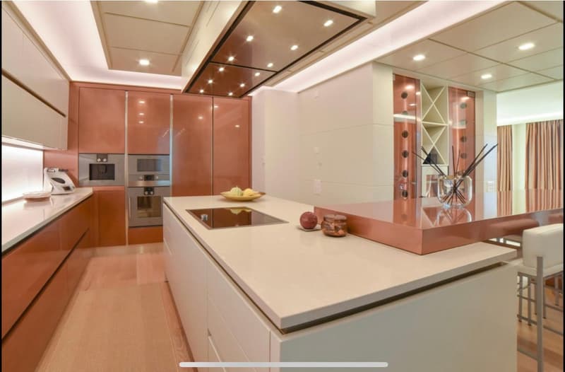 Spacious modern kitchen with sleek orange cabinets, white countertops, built-in appliances including a dishwasher, and decorative lighting fixtures.