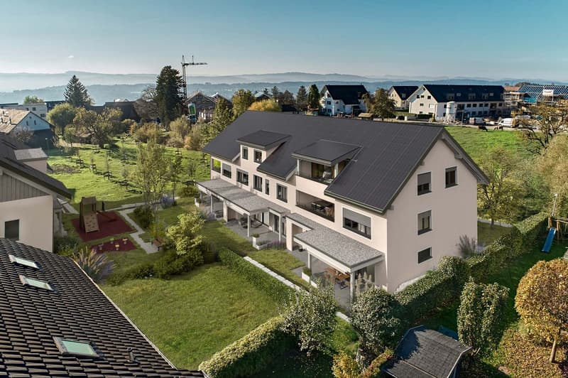 4-story apartment building with black roof tiles, white exterior, and balconies. The building is surrounded by a well-maintained lawn and landscaping, with other residential buildings visible in the background. The setting appears to be in a suburban or s