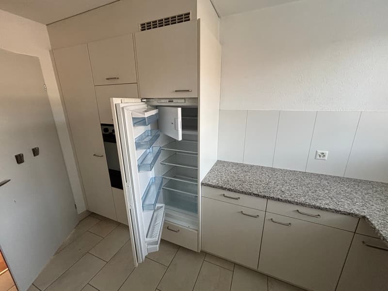 The image shows a kitchen with white cabinets, a granite countertop, and a refrigerator. The kitchen appears to have a private washing machine and a dishwasher.
