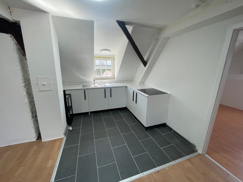 Compact kitchen with gray cabinets, black tile flooring, and a window providing natural light. The kitchen appears to have a dishwasher installed.