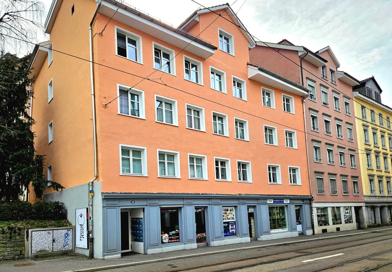 A multi-story building with multiple windows, painted in a peach color, with a shop on the ground floor.