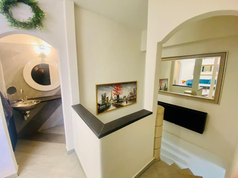 Bathroom with sink, mirror, and painting, mirror reflection showing stairs and sitting area.