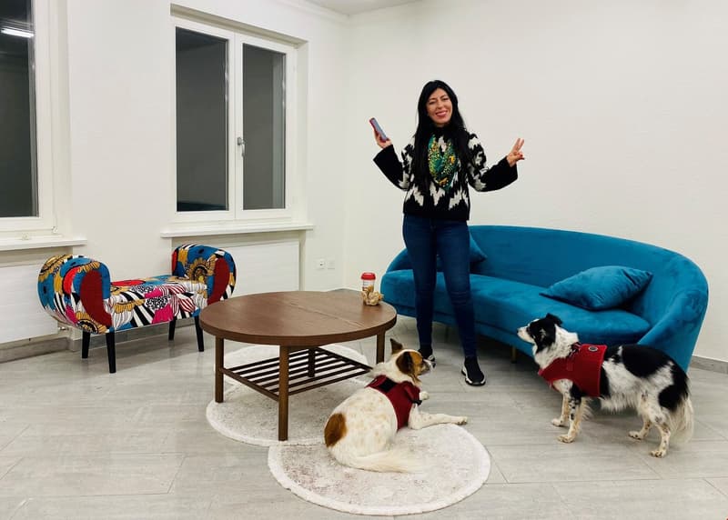 living room: carpet, coffee table, couch, armchair, white walls, windows, person with dogs