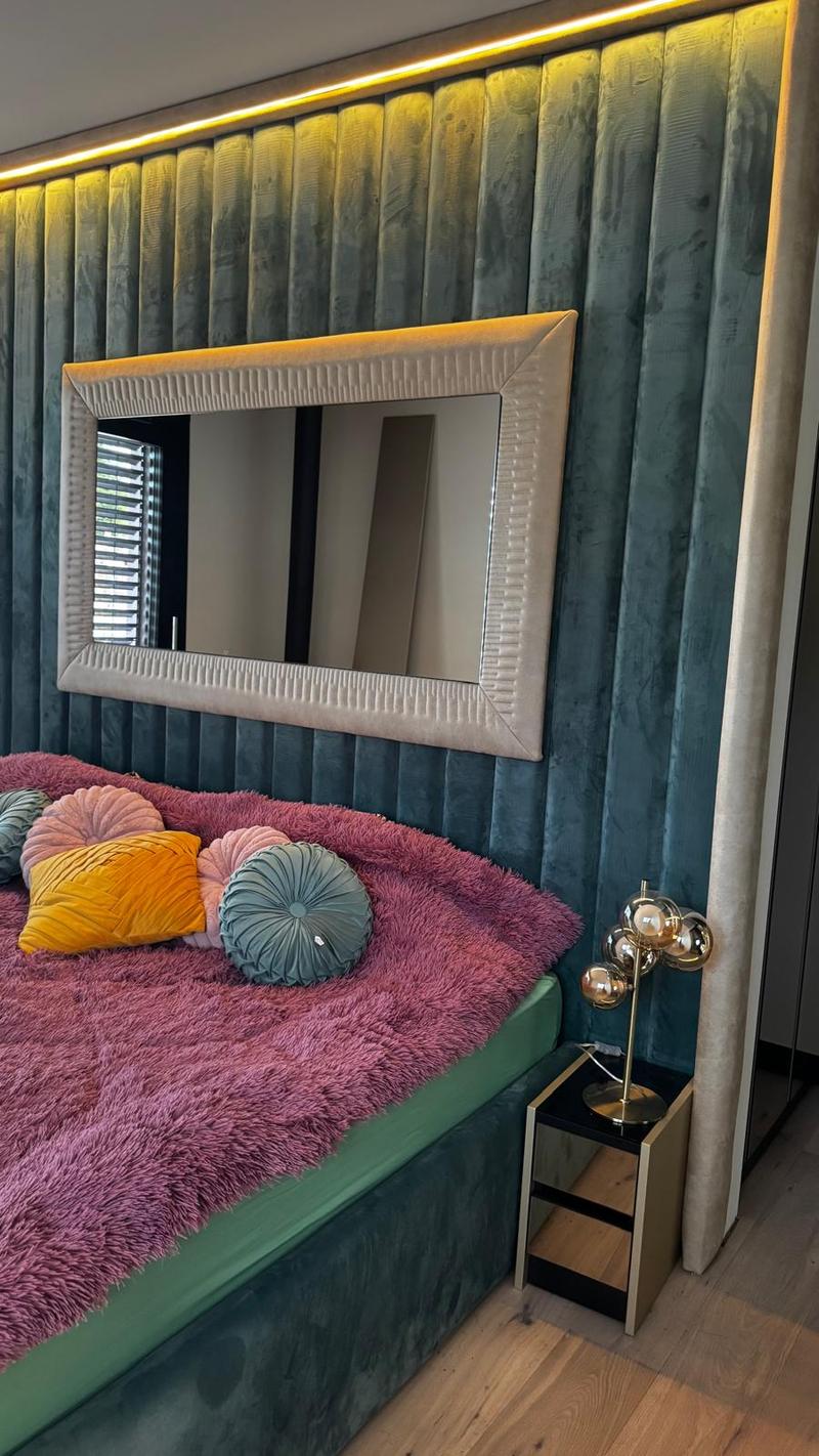 modern bed with pink fur blanket, decorative cushions, night table with lamp, large mirror