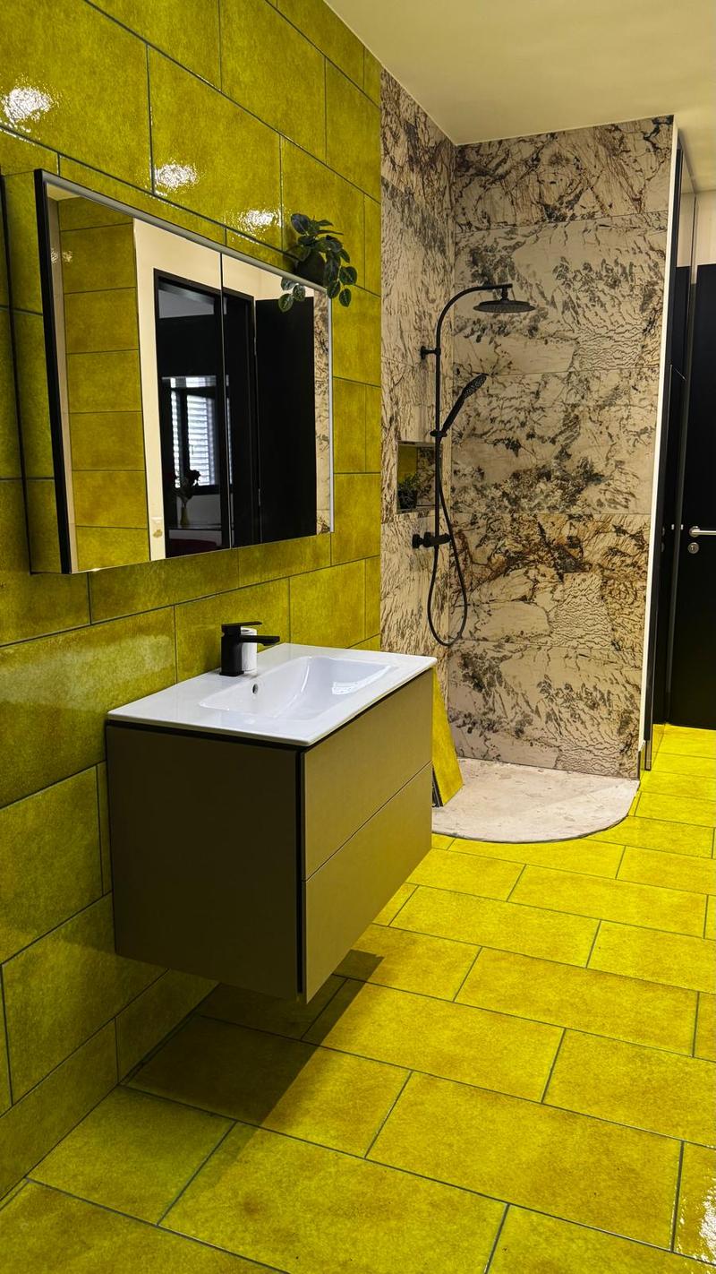 bathroom with bright yellow tiles, mirror with cabinet, white vanity with sink, black showerhead, potted plant in corner
