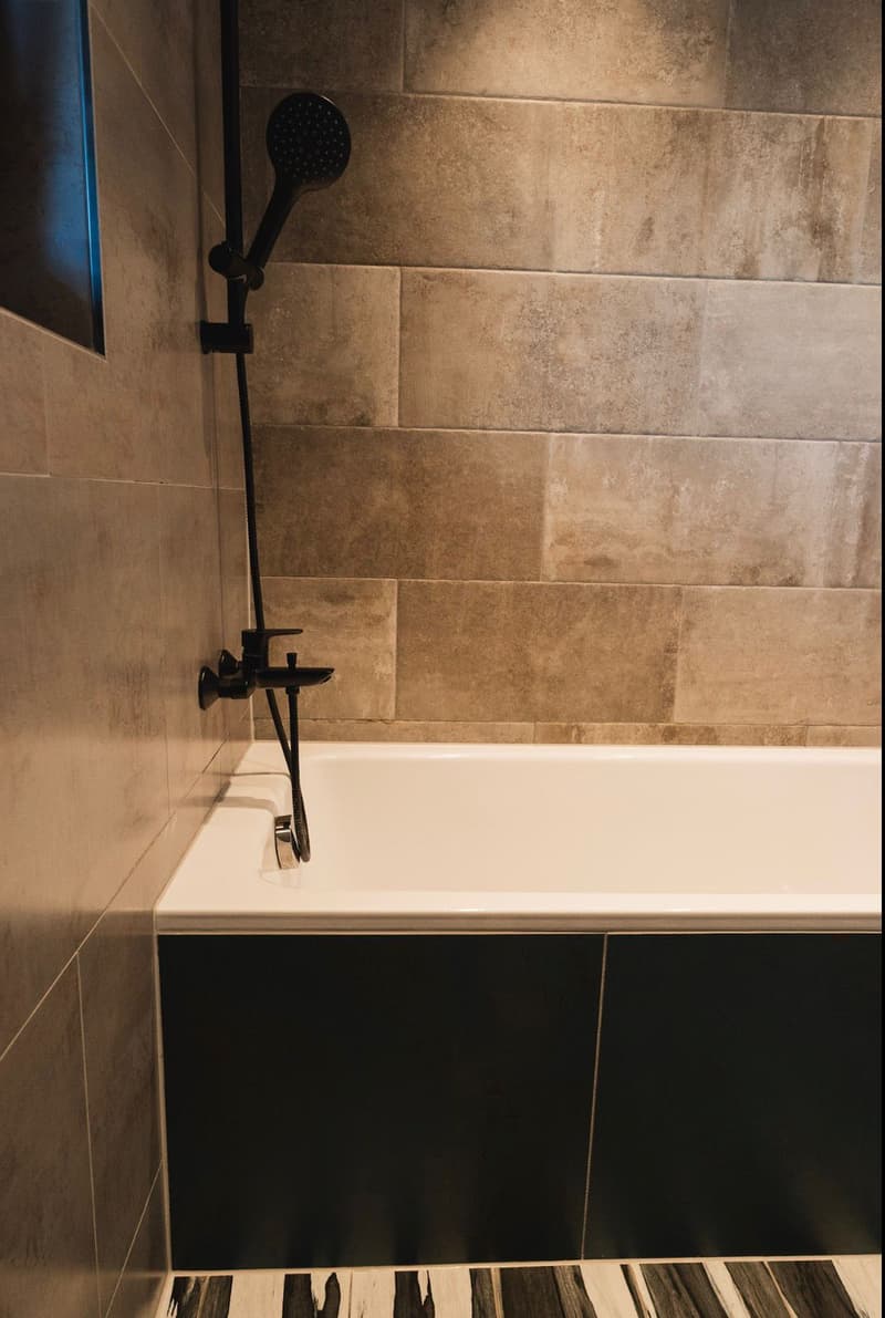 Bathroom with bathtub, shower head, tiled walls, black and white floor