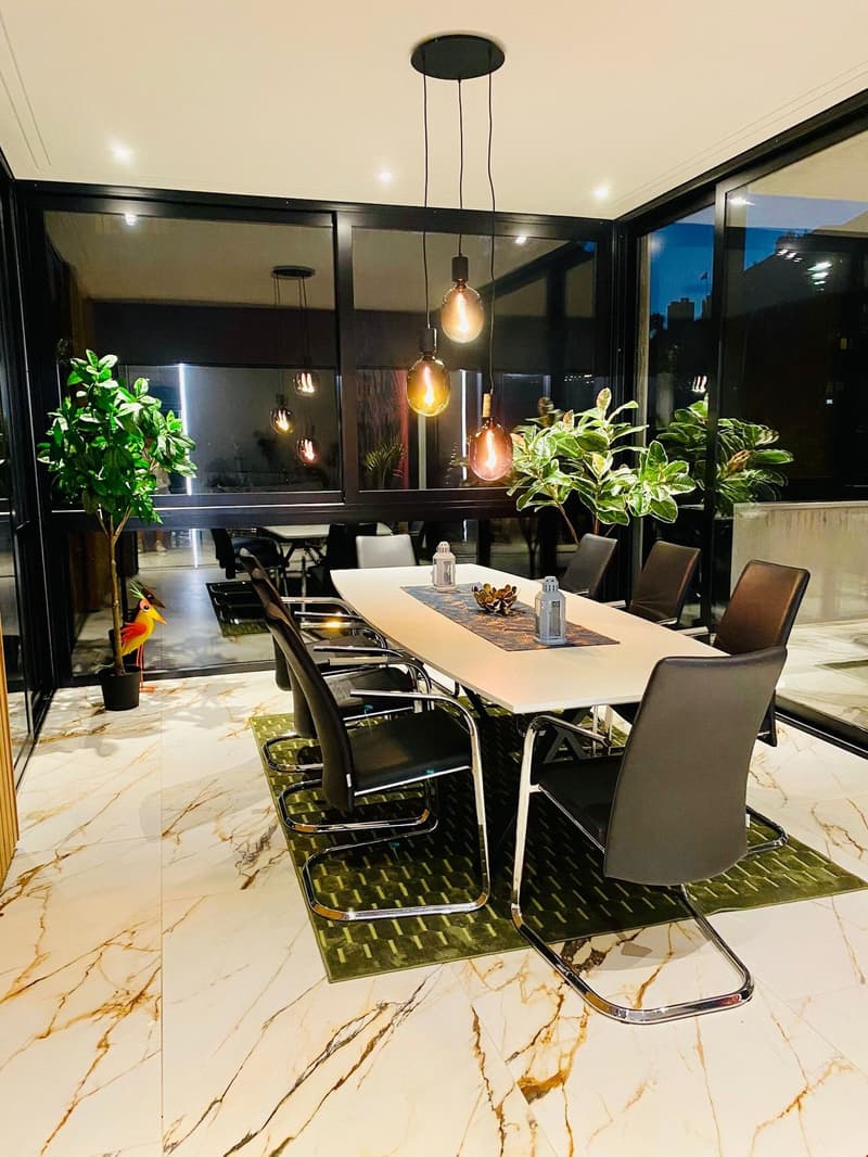 Marble floor, large glass windows, pendant lights, large dining table with chairs, plants, large decorative plate