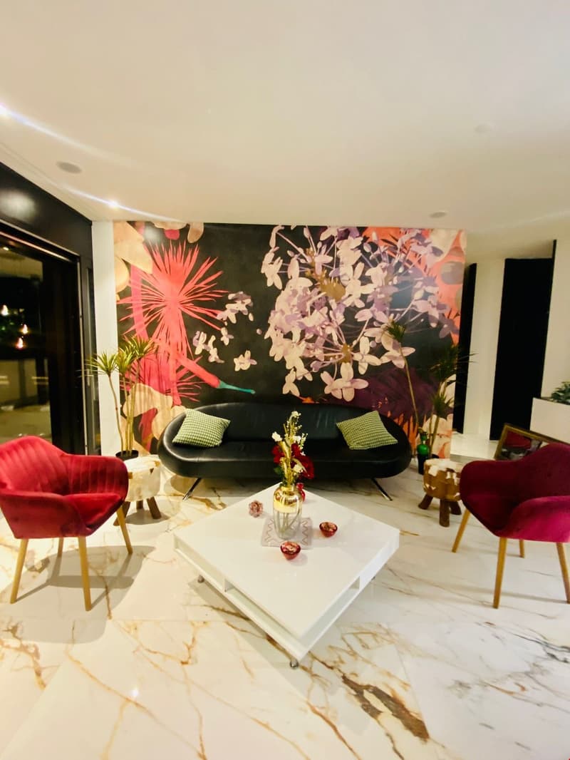 Black sofa, red chairs, white marble floor, large decorative floral wall art, central coffee table, plants, and various decorative items on the table.
