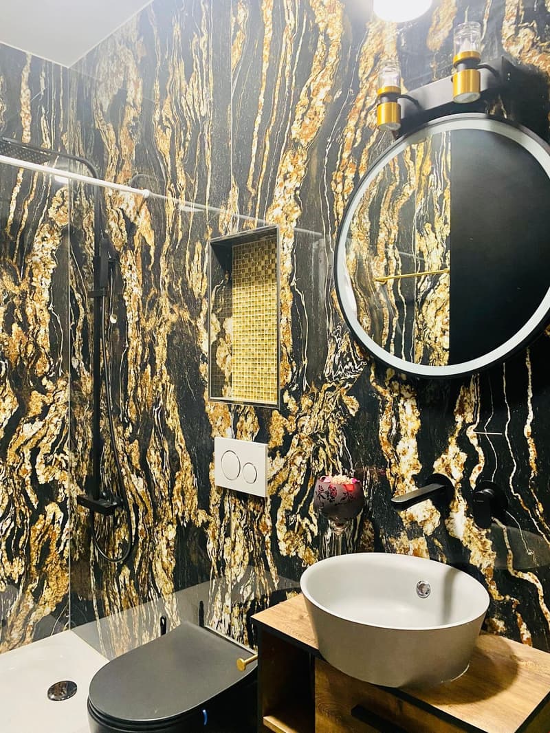 Marble wall with gold veins, round mirror, large round sink, glass shower stall, modern toilet