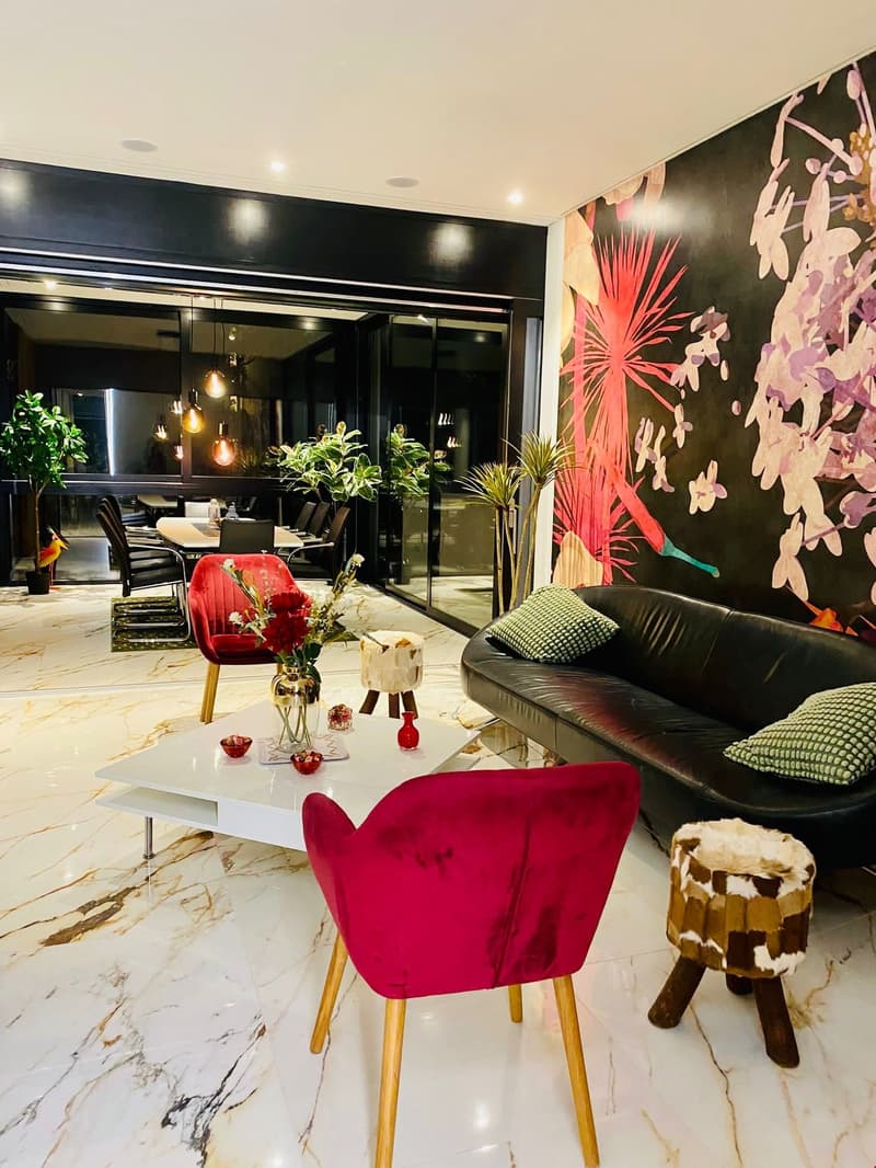 black leather couch, white coffee table, red armchairs, flower vase, patterned rug, potted plants, black walls, floral mural