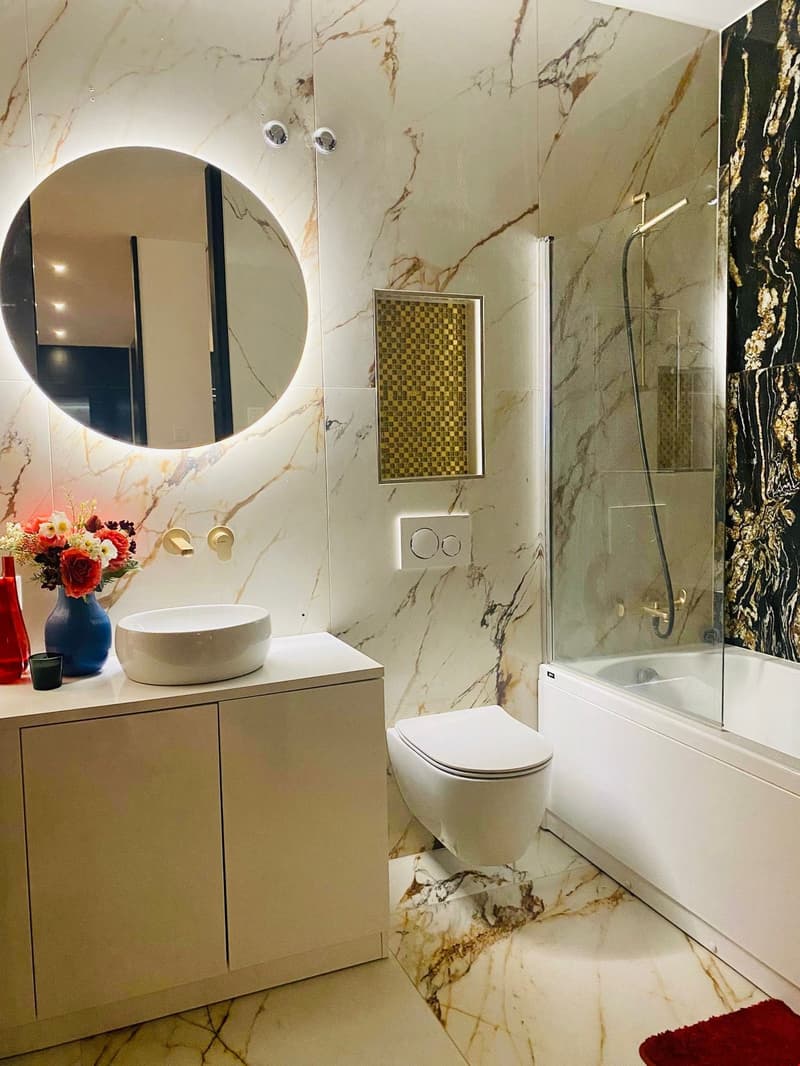 Circular marble-like walls, white floor tiles, round sink with a round mirror, modern white toilet, and a walk-in shower.