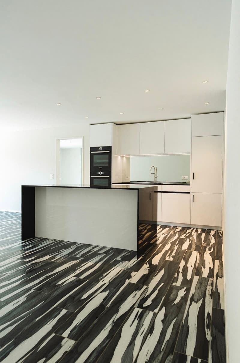 modern kitchen with white cabinets, black and white tiled floor, island with black countertop, double oven, sink with faucet, mirror