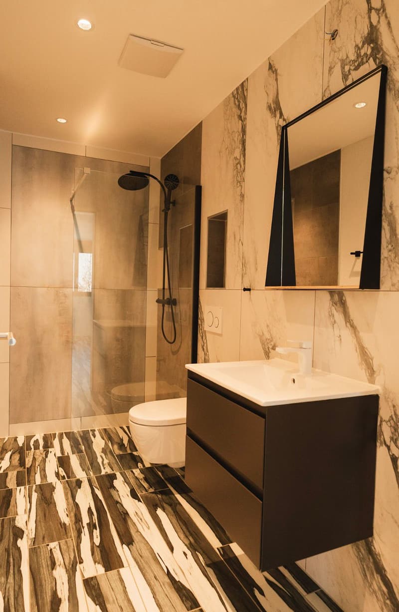 modern bathroom with marble walls, glass shower enclosure, white toilet, white sink, black cabinet, mirror
