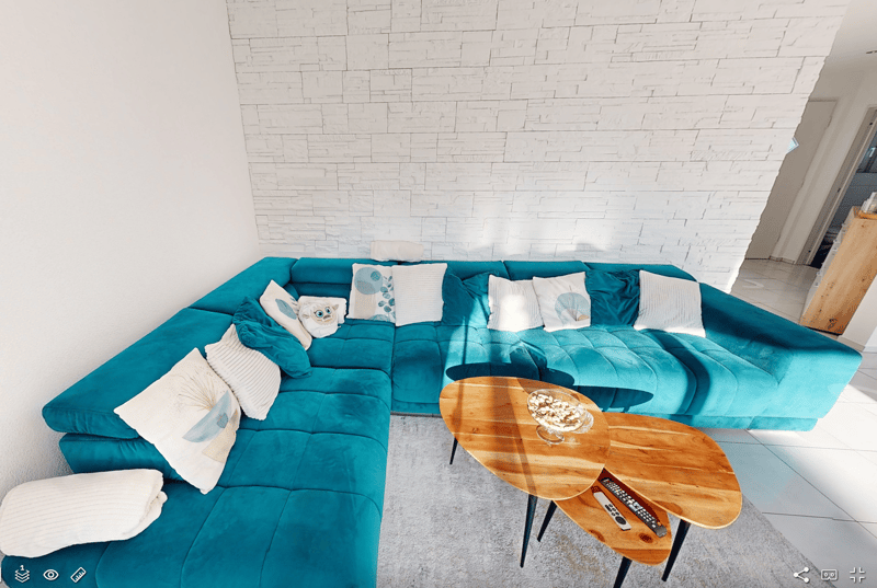 A living room featuring a large blue L-shaped sectional sofa, wooden coffee tables, white walls, and white tiled flooring.