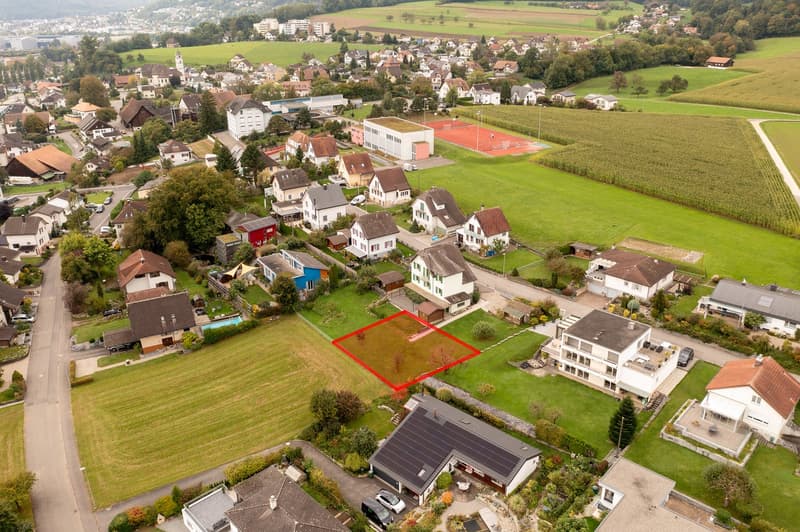 Suburban neighborhood with various sized houses, one empty plot marked with red rectangle, houses have various features like garages and solar panels
