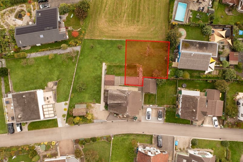 An aerial view of multiple residential properties in a suburban area. There are multiple detached houses with solar panels, some with garages. A central lot is highlighted by a red outline, indicating it is likely the subject of sale or development.