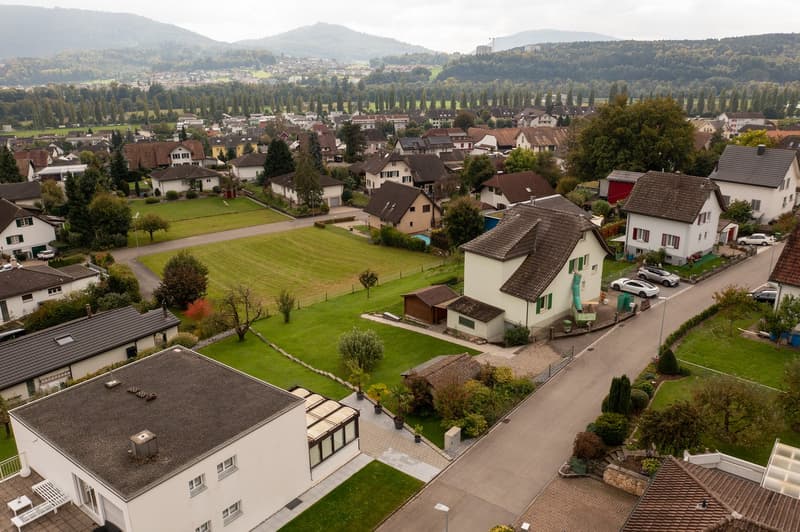 Aerial view of a town with residential houses, trees, mountains, open fields, street with parked cars