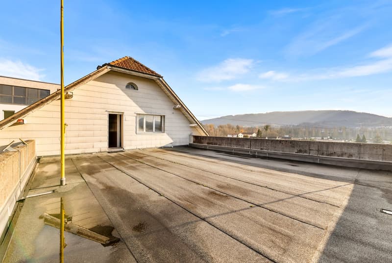 Concrete rooftop with surrounding walls, yellow pole, distant houses and mountains