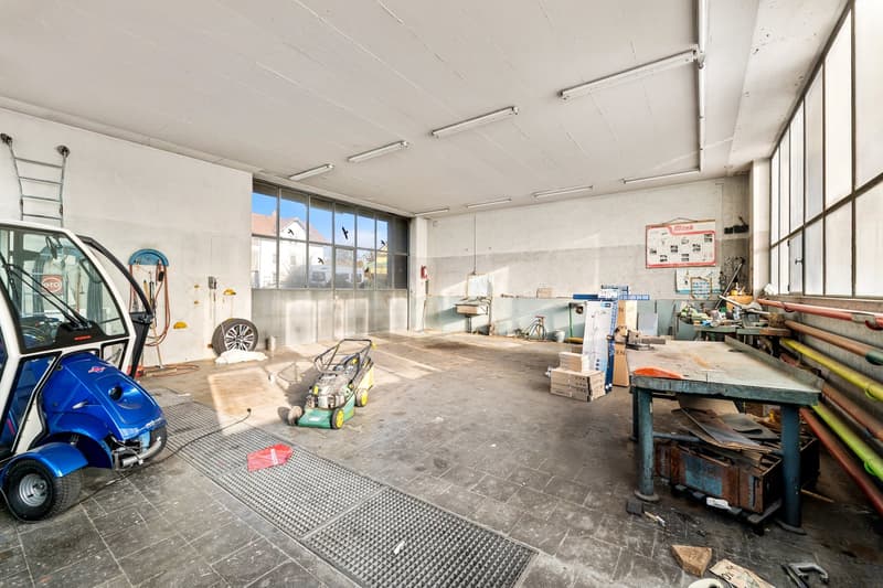 Garage with several workbenches, equipment, storage boxes, tires, small wheeled car, and glass wall
