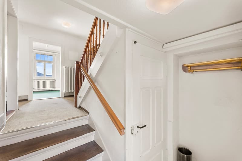 Empty corridor with wooden staircase, white walls and ceiling, radiators, a view from the stairs