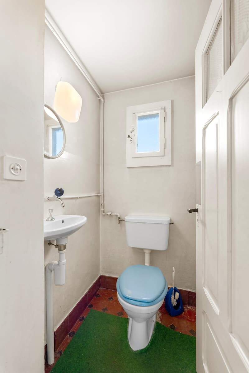 Small bathroom with toilet, sink, mirror, and small window