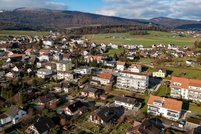 cluster of residential buildings with varying sizes and architectural styles, surrounded by greenery and hills