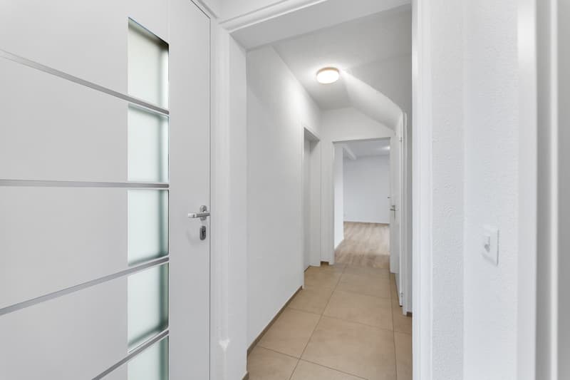 Empty hallway with white walls, tiled floor, glass door, and ceiling light