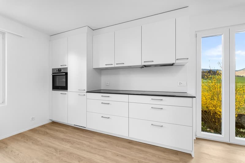 modern kitchen with white cabinets, black countertops, built-in oven, large windows