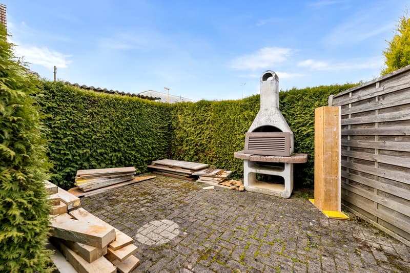 brick paved area, outdoor fireplace, wooden fence, green hedges, wooden planks