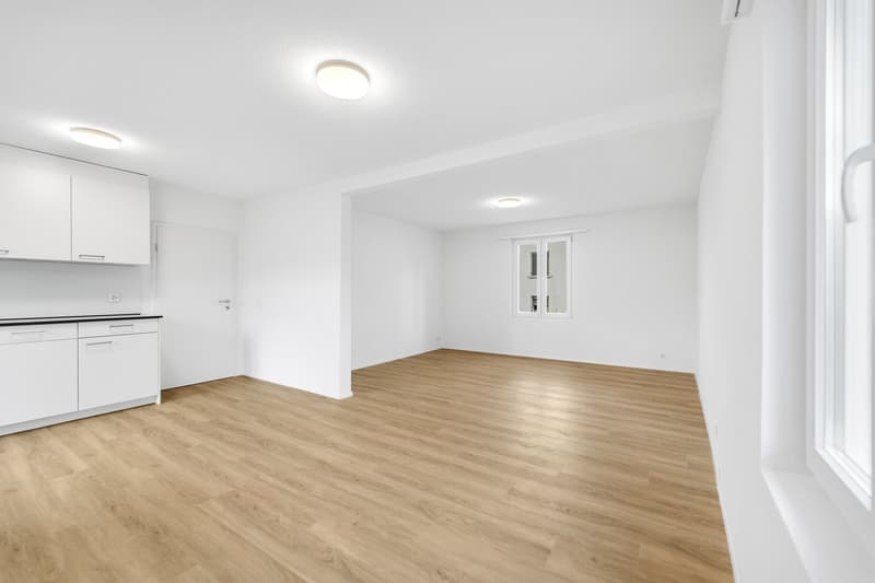 Empty room with white walls, wooden floor, white cabinets, and windows