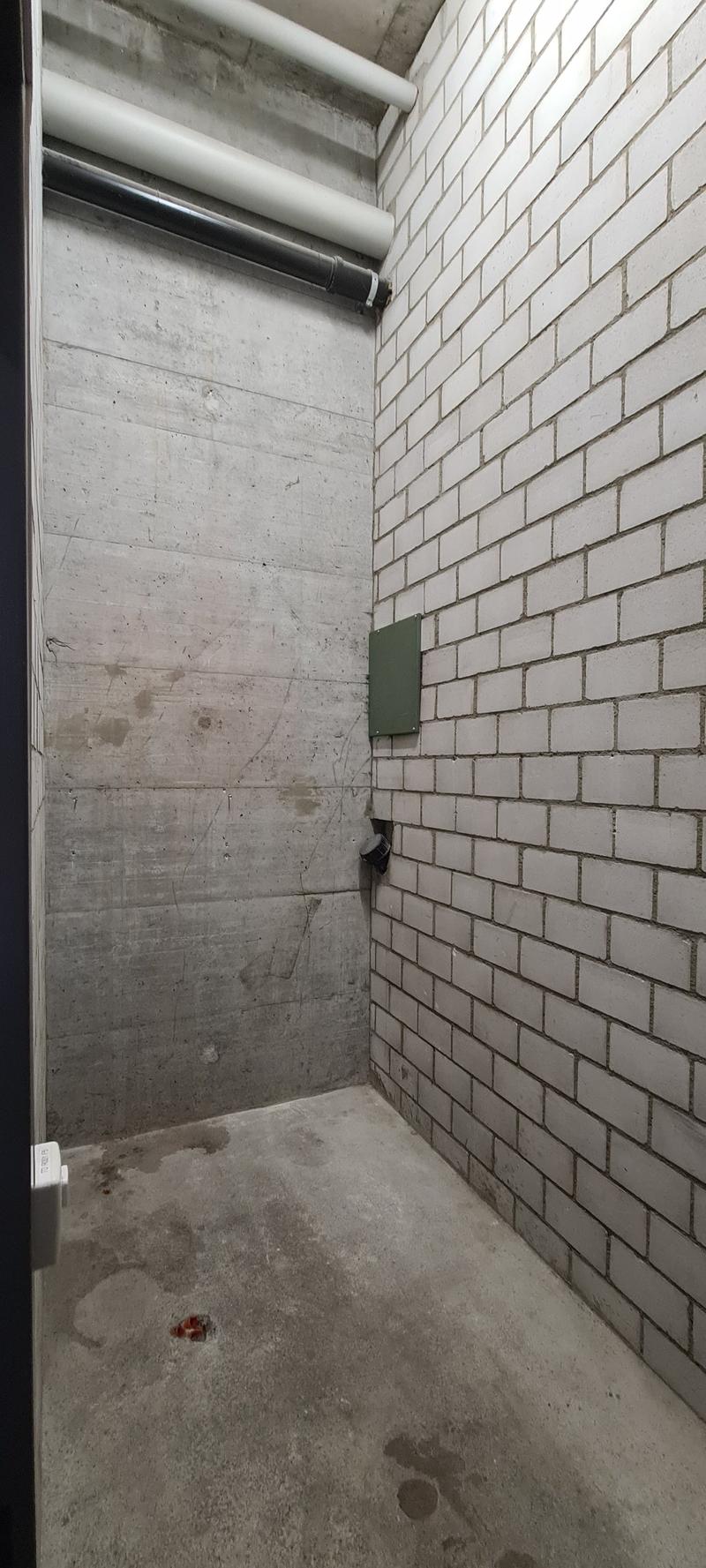 Concrete walls, unfinished floor, exposed pipes, and a small electrical box on the wall.