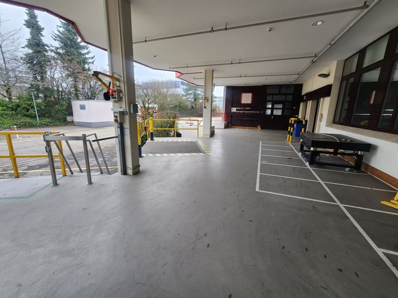 empty concrete ground floor with yellow railings, large empty parking area, windows, poles, machinery, metal stairs
