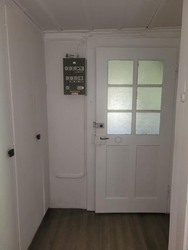 Small room with white walls, a white door, and a washing machine on the wall.